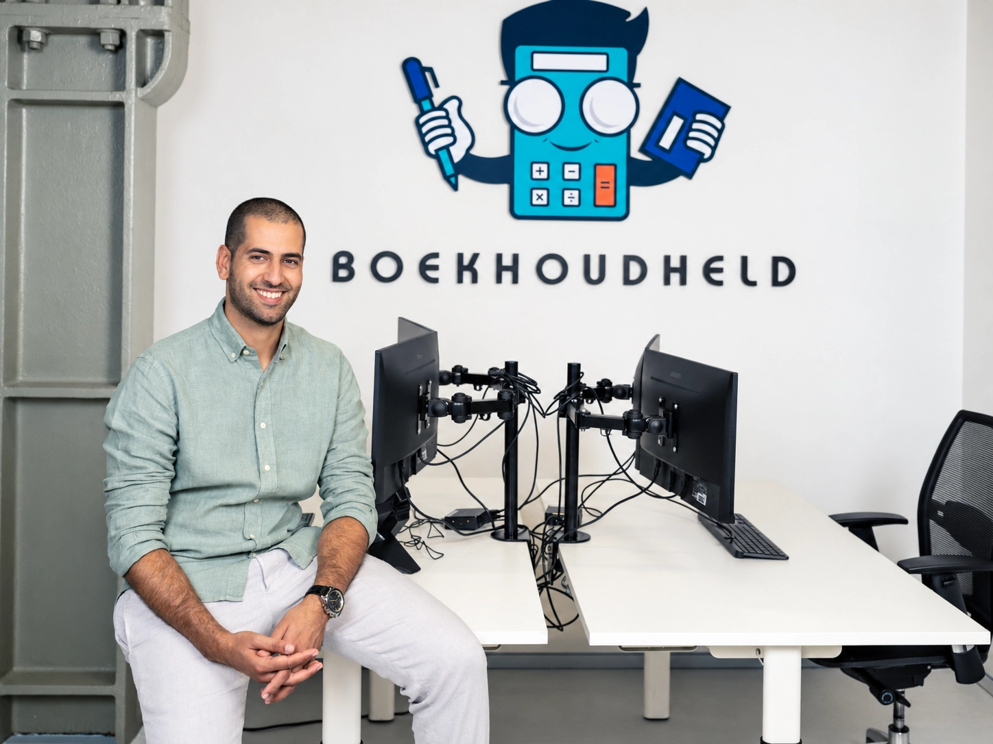 Anass Bounhilat in het eerste kantoor van Boekhoudheld, bij de logowand