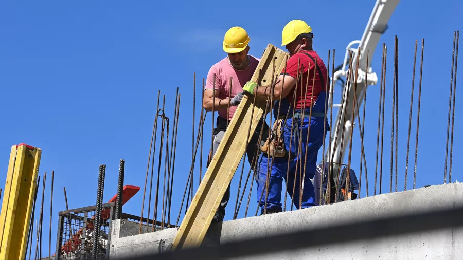 Twee bouwvakkers met helmen werken aan een betonnen vloer met wapeningsstaal