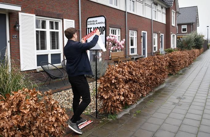 Makelaar plaatst een verkocht-sticker op een verkoopbord voor een woning