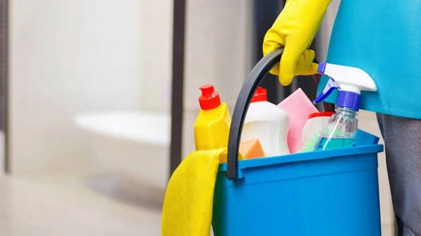 Schoonmaker met handschoenen draagt een emmer met schoonmaakmiddelen